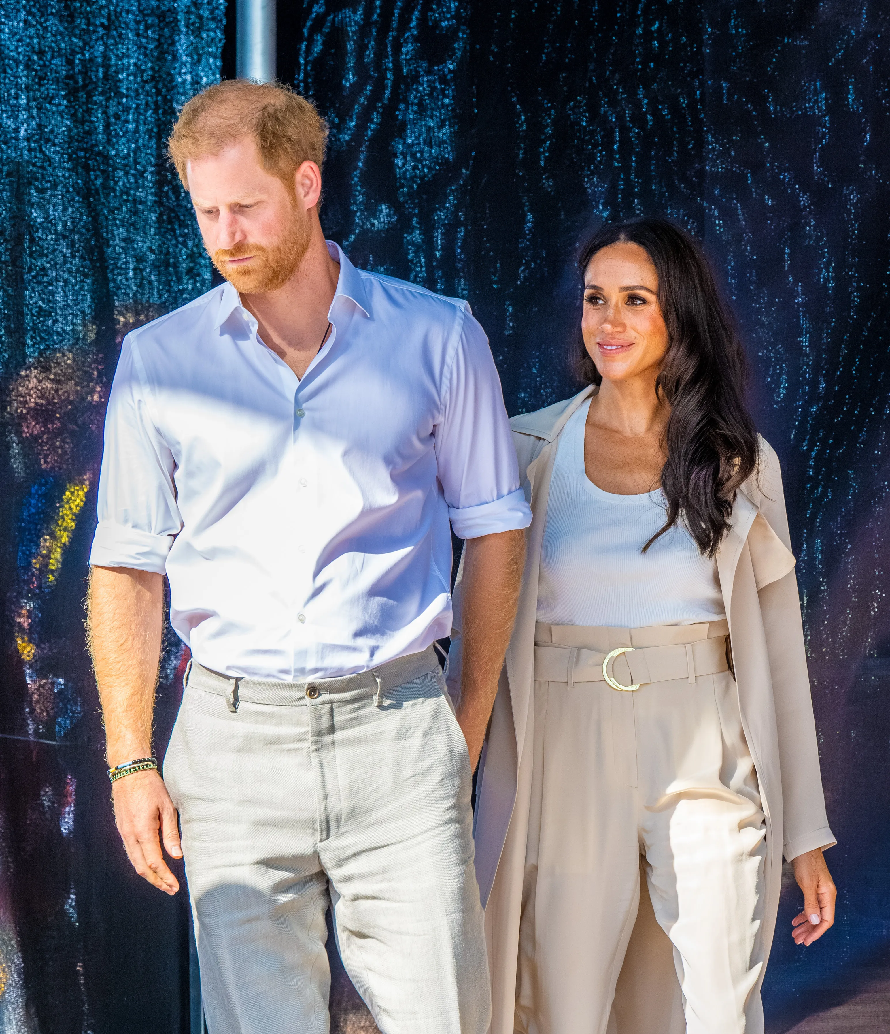 Meghan Markle and Prince Harry stand side-by-side with a dark, glittering background.