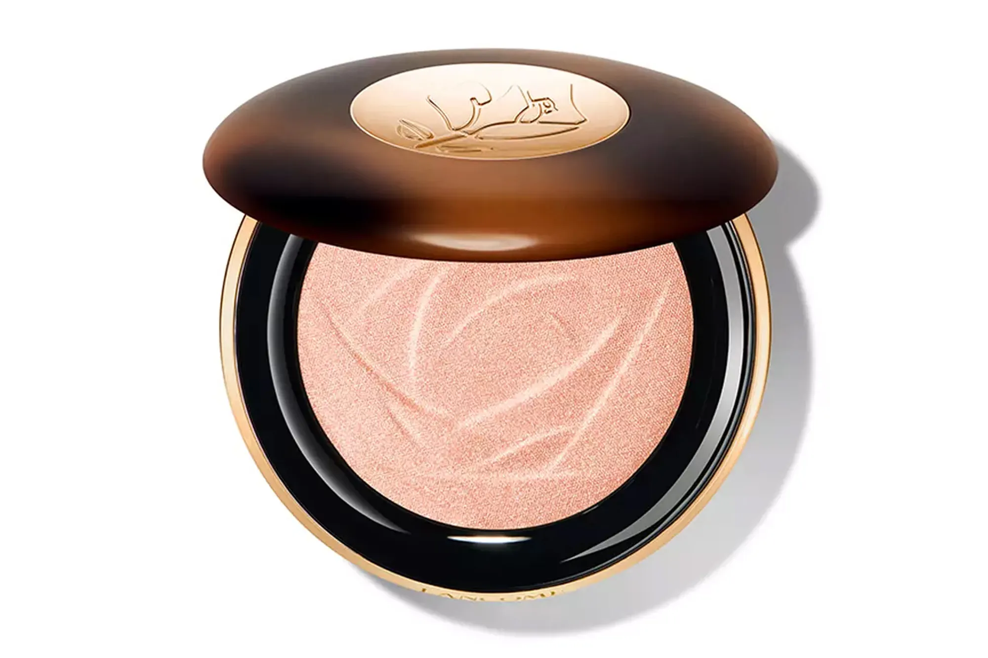 Open compact with peach-toned powder highlighter featuring a subtle rose design, set in a gold and black case with a brown lid.