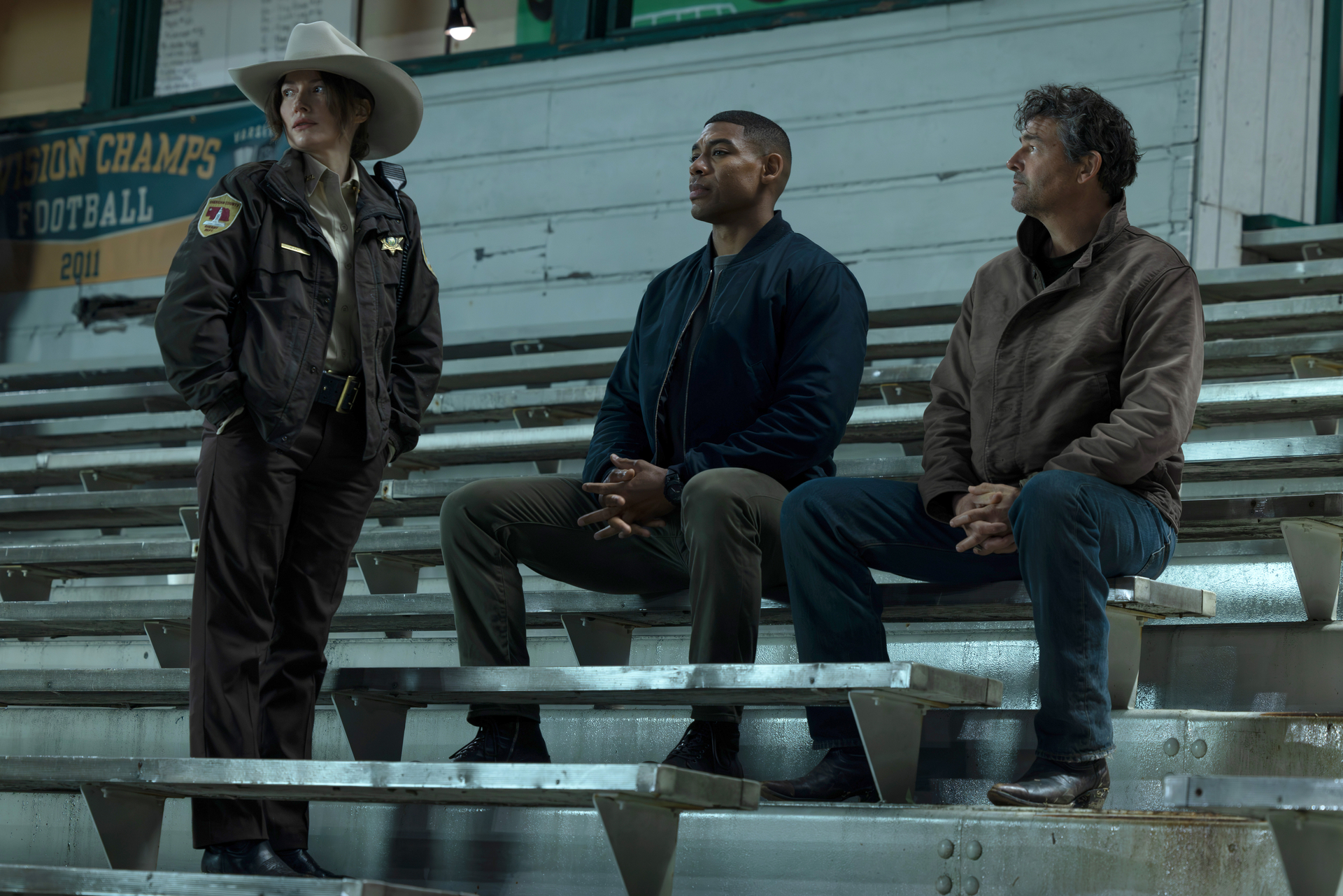 Kyle Chandler, Aaron Pierre, and another actor on bleachers in the HBO show "Lanterns."
