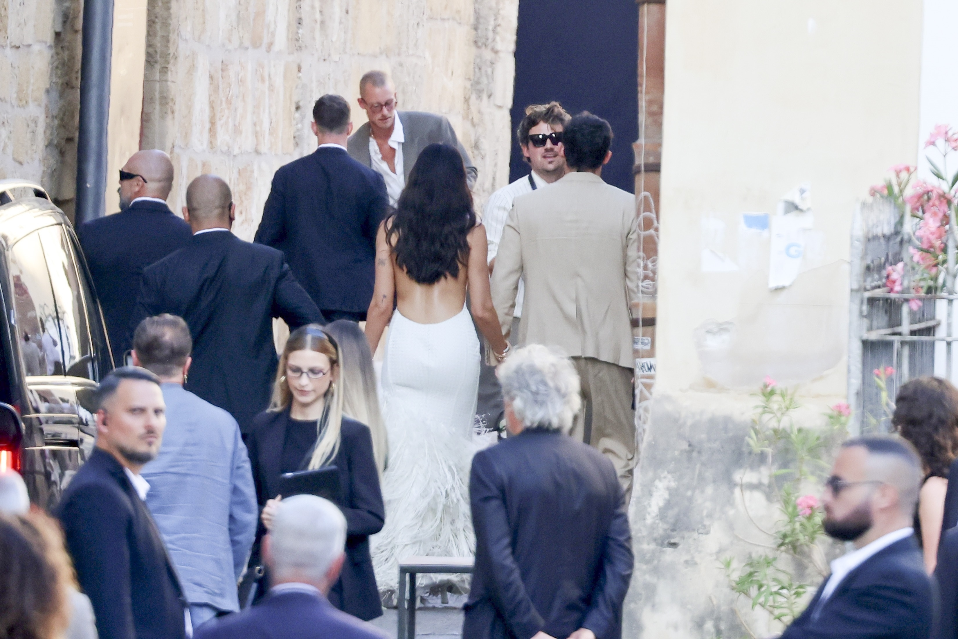 Dua Lipa in a white gown and Callum Turner in a tan suit arriving with family at G.A.M. in Palermo.