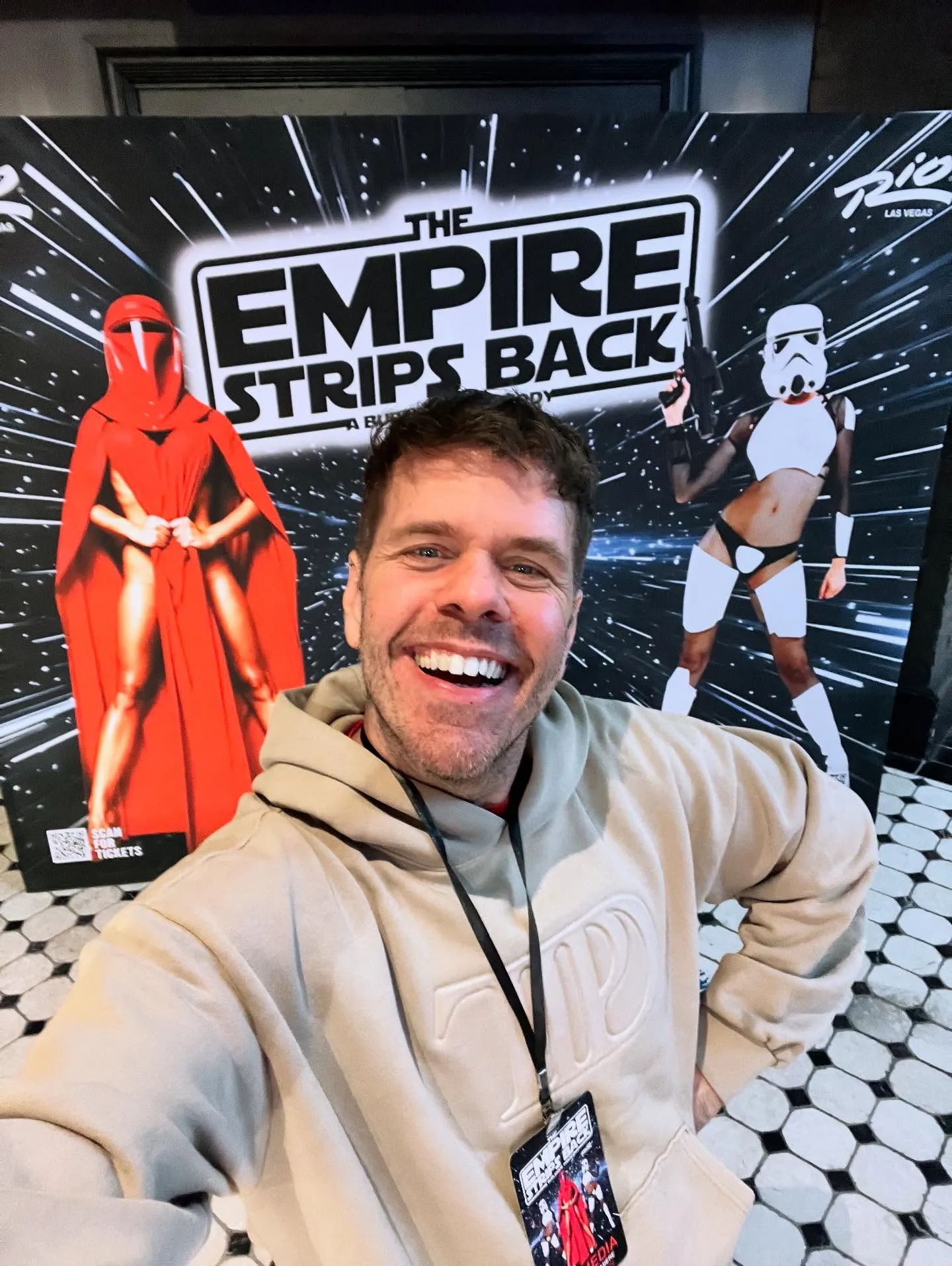 smiling in front of a poster for "The Empire Strips Back."