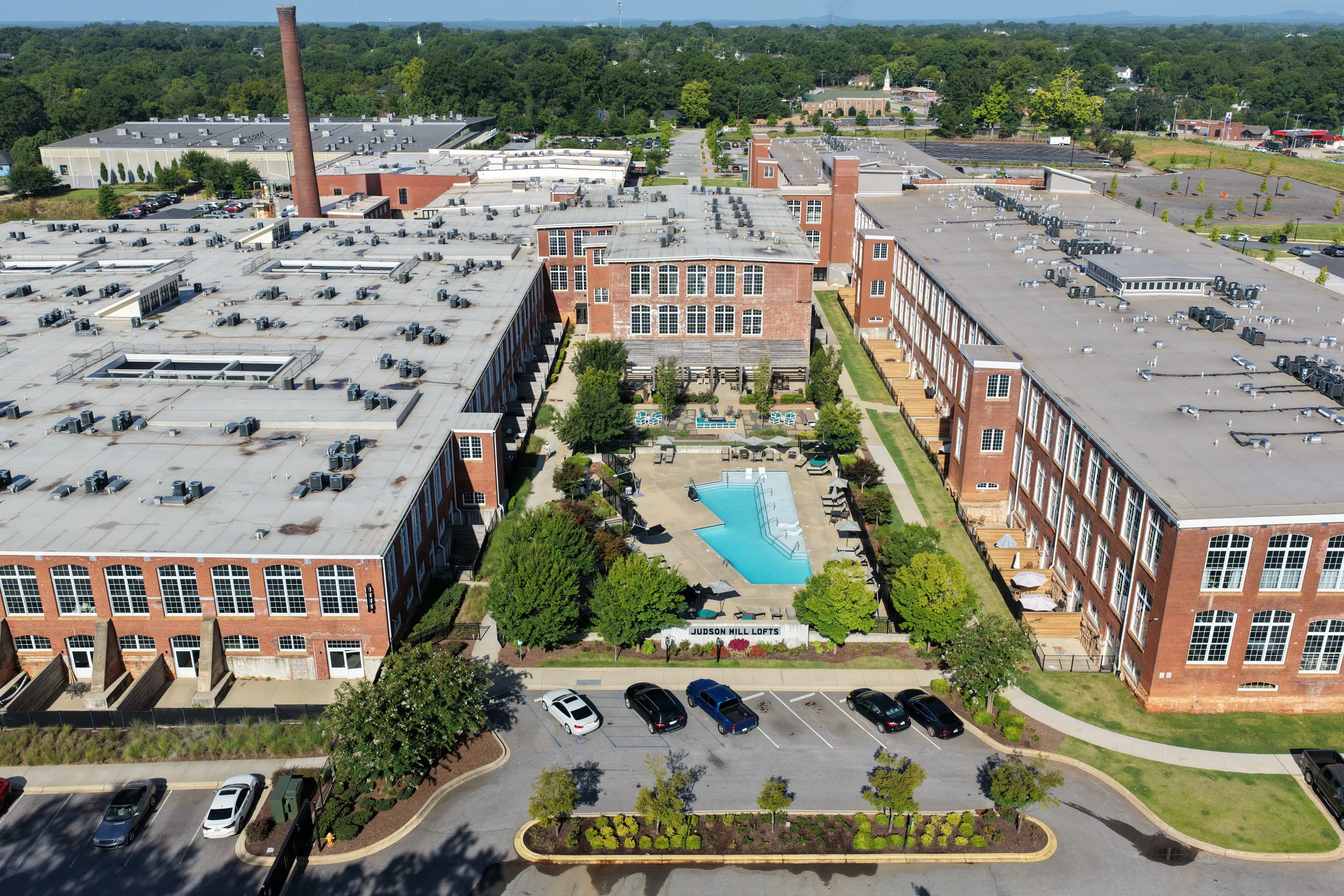 Aerial view of the Judson Mill Lofts apartment complex, featuring brick buildings, a swimming pool, and parking lots.