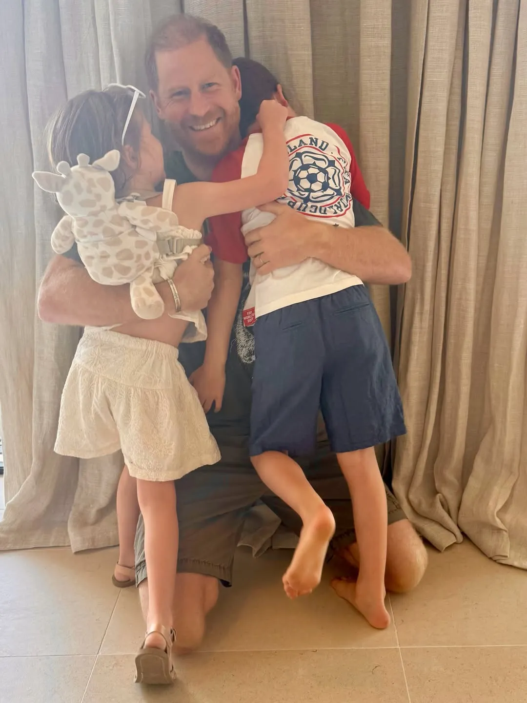 Prince Harry kneeling and embracing his children, Prince Archie and Princess Lilibet.
