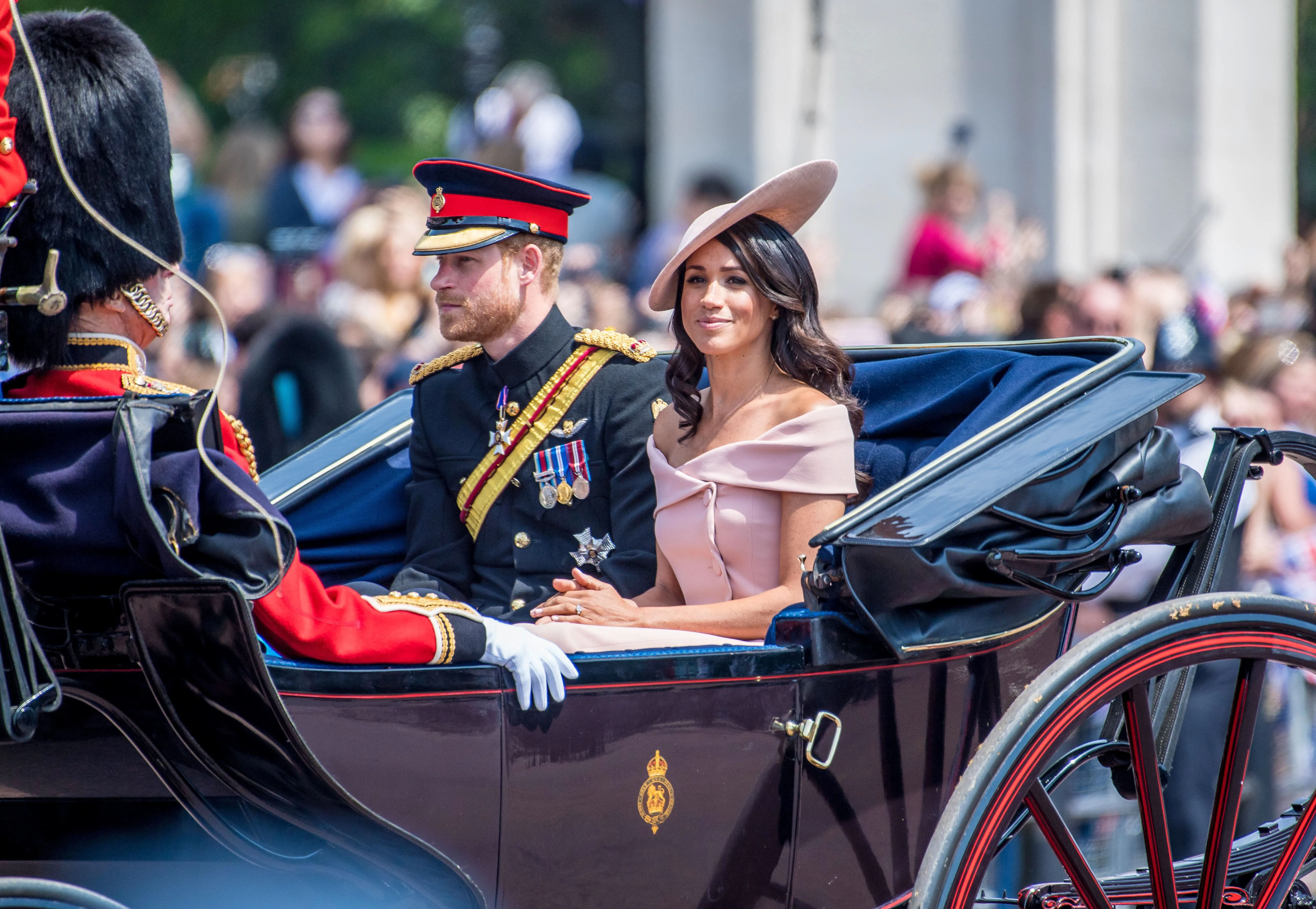 Prince Harry and Meghan Markle riding in a horse-drawn carriage during a public event.