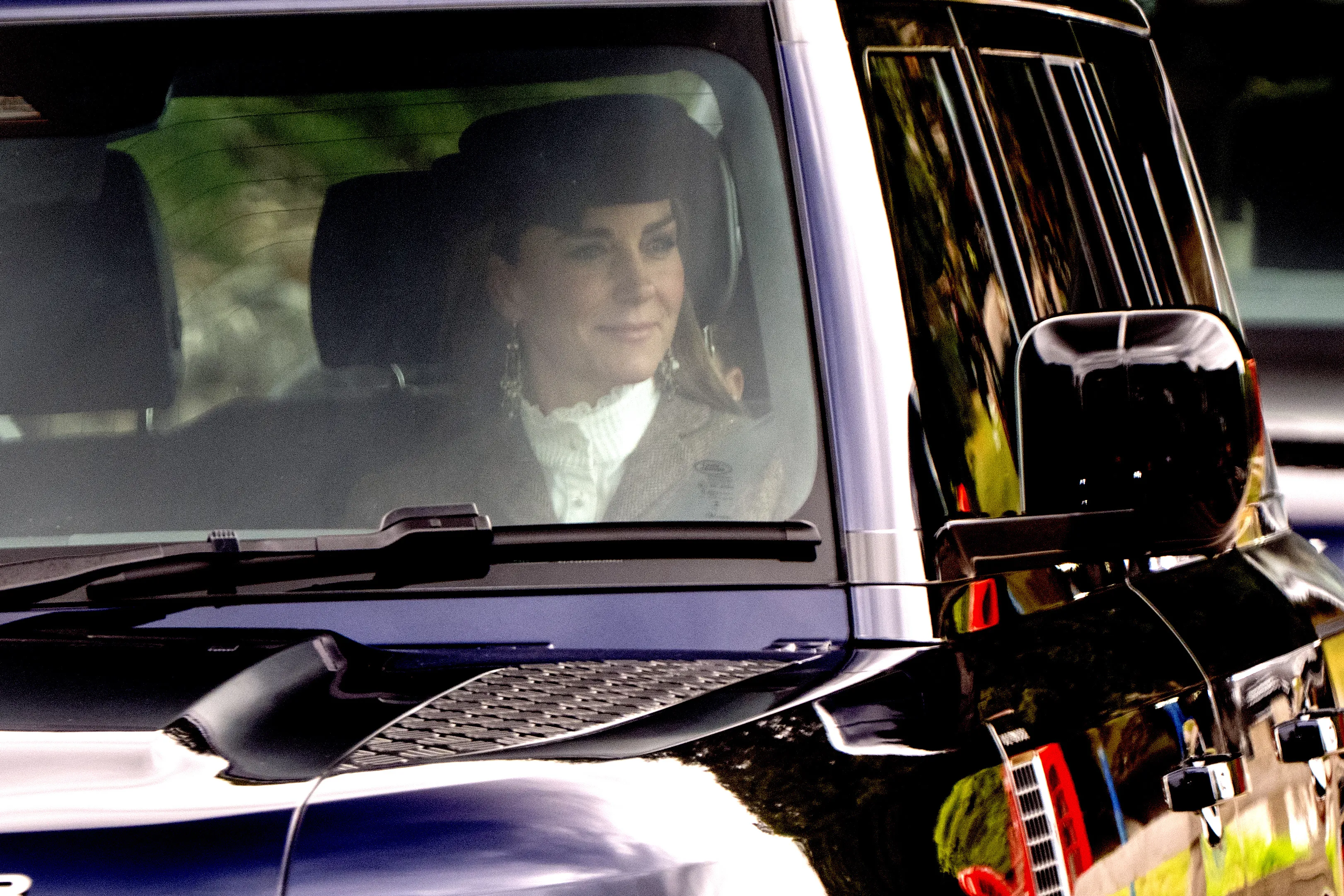 Catherine, Princess of Wales, in a hat and white ruffled blouse, looks out from a car window.