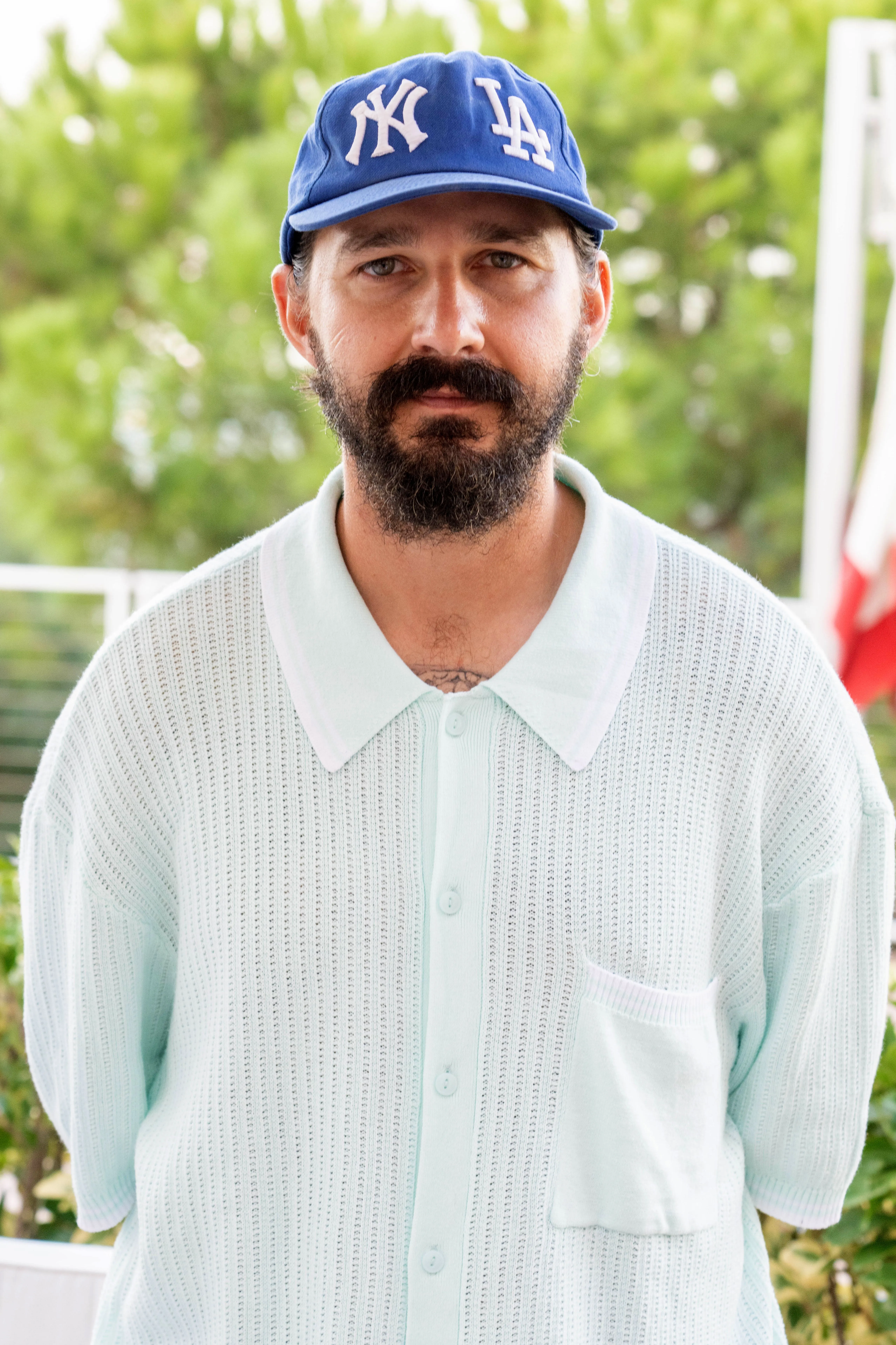 Actor Shia LaBeouf wearing a blue baseball cap and light blue collared shirt.