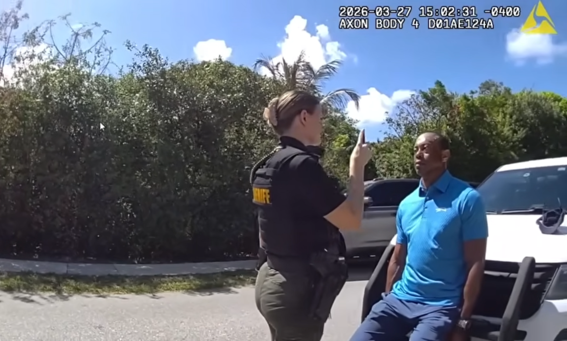 Tiger Woods sitting on the bumper of a police car with a female officer standing in front of him.