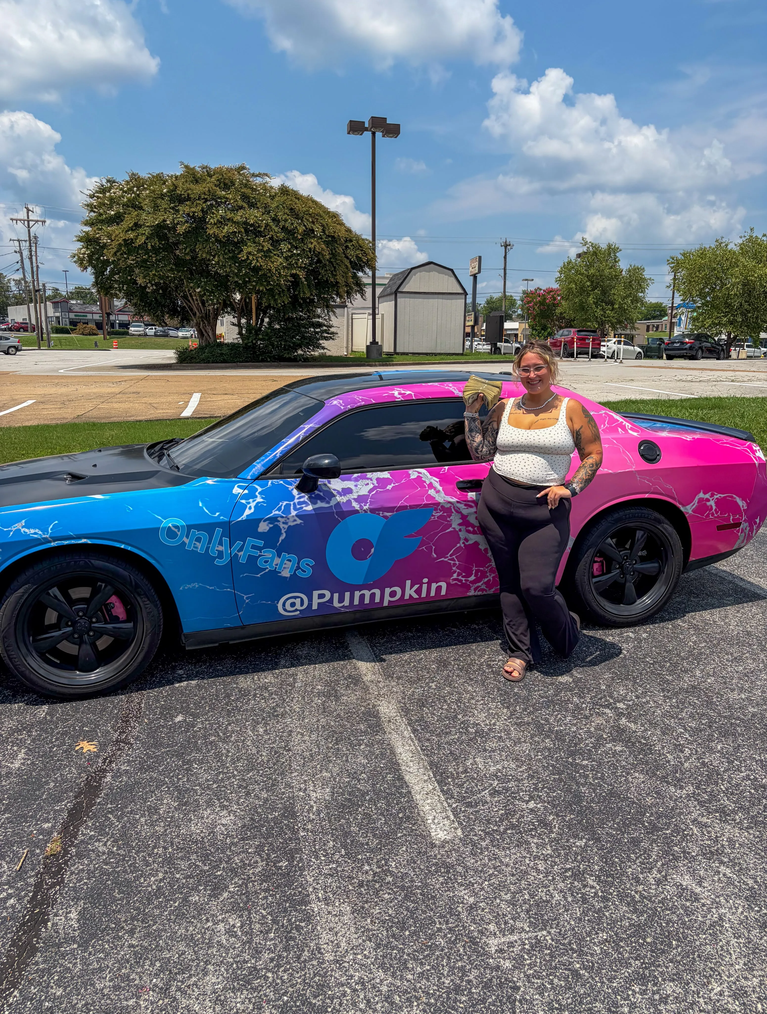 A woman holding a stack of money next to a car with "OnlyFans @Pumpkin" written on it.
