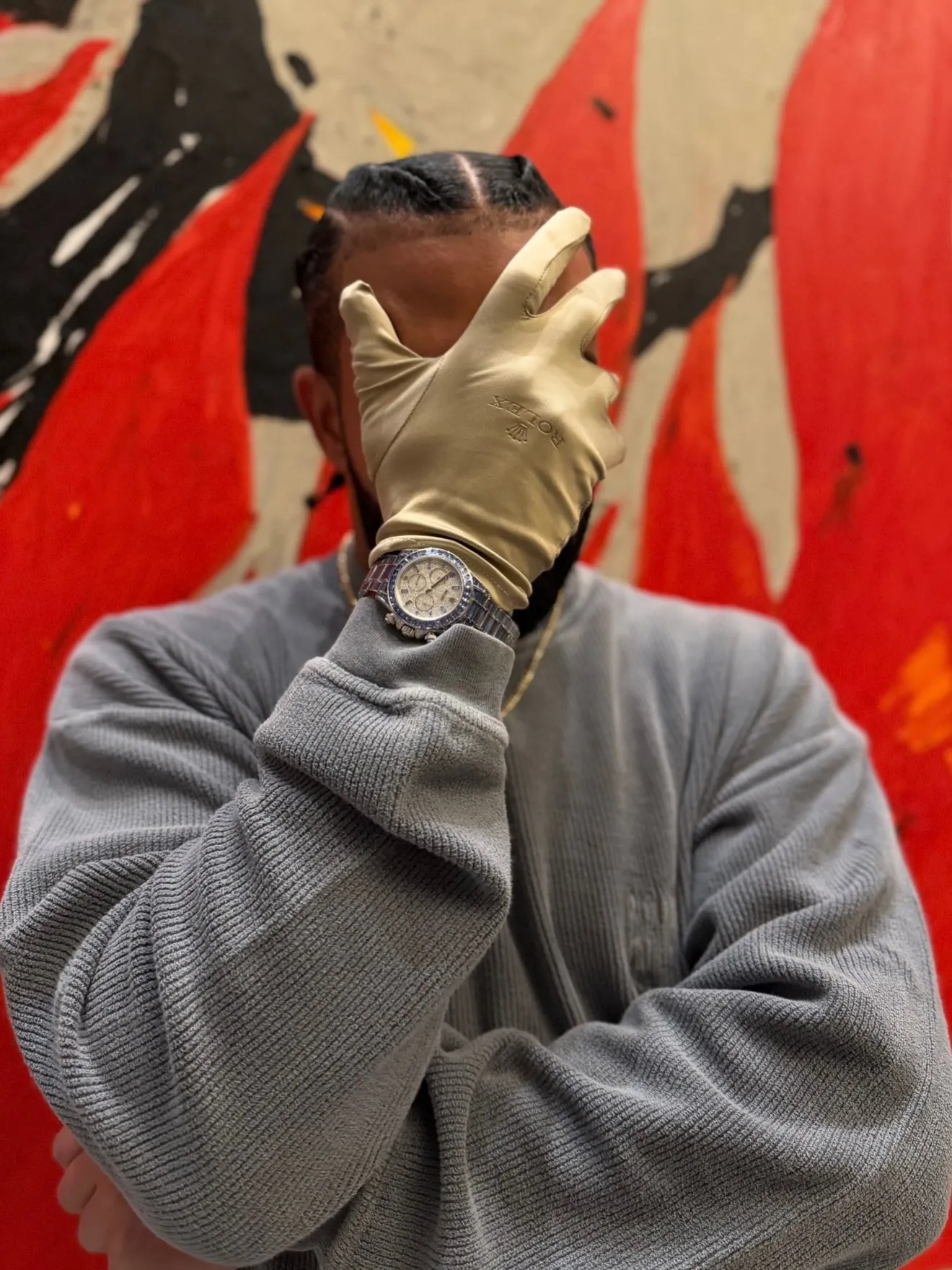 A person wearing a golden glove with a Rolex logo and a Rolex Daytona watch on their wrist.
