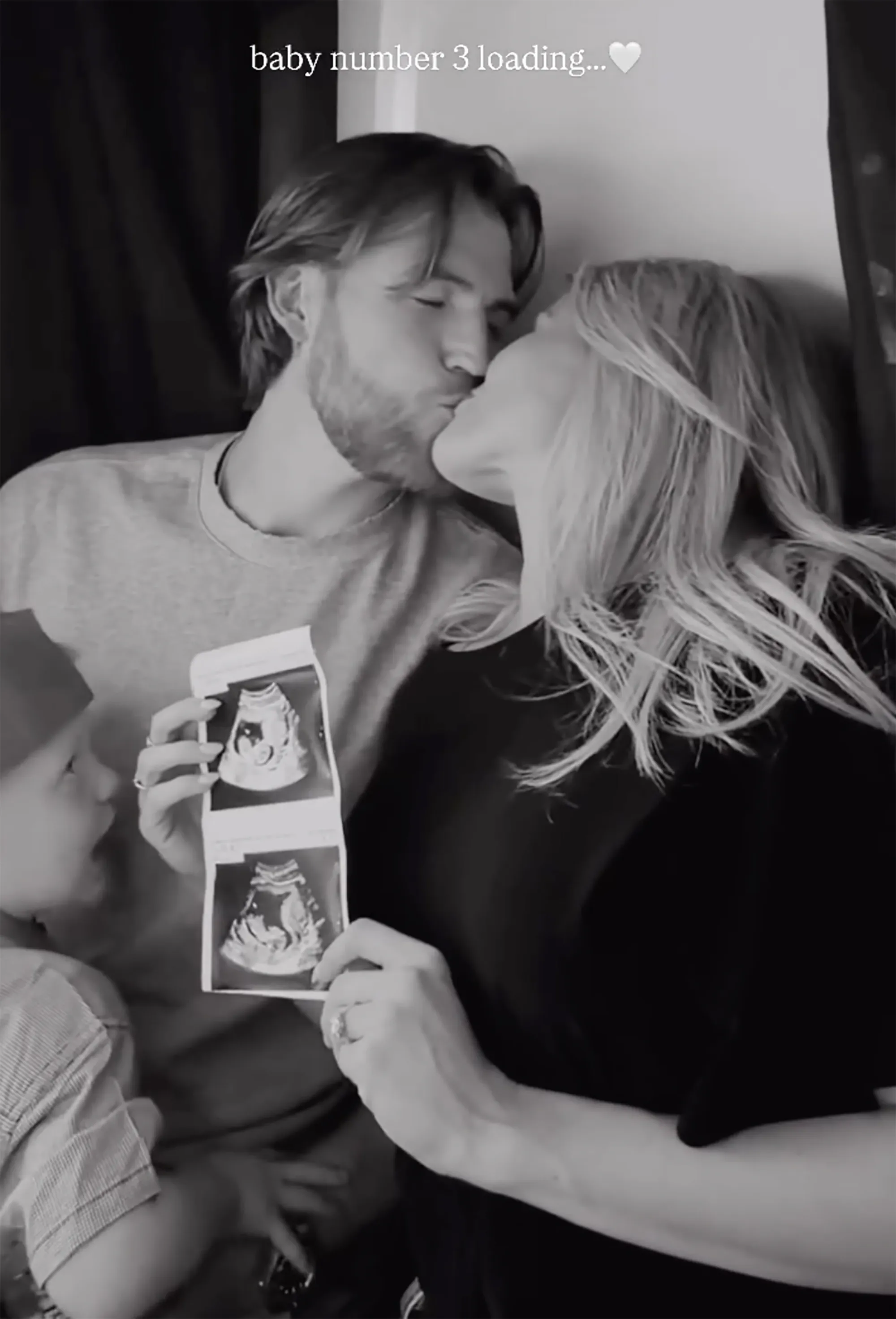Black and white photo of Witney Carson and her husband kissing, holding up ultrasound photos, and her child looks on.