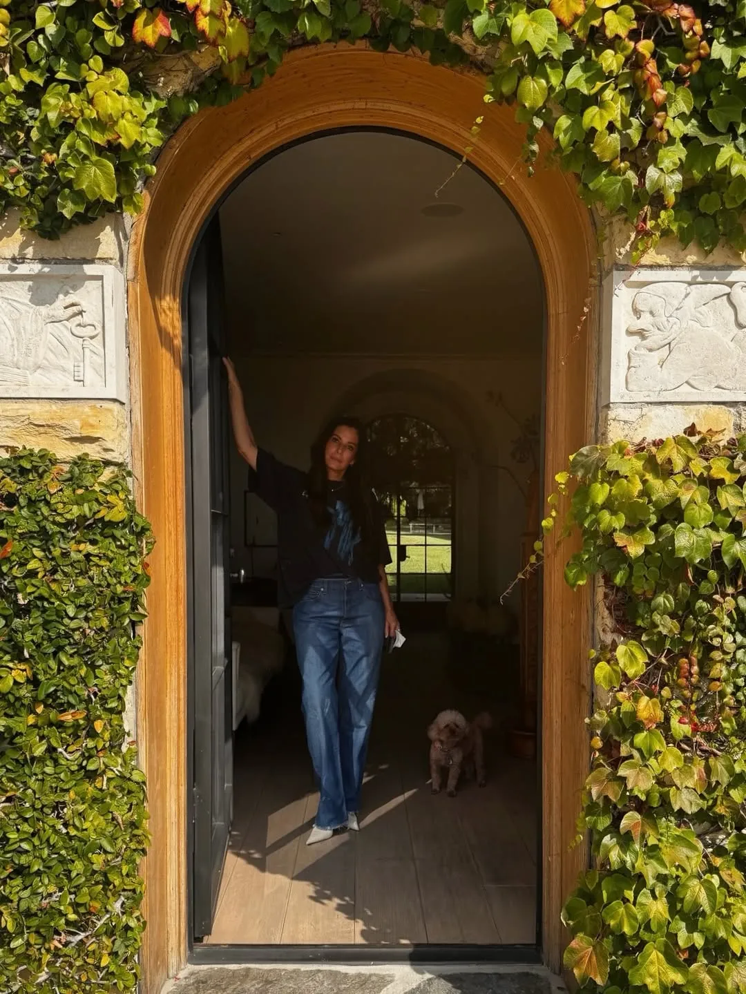 Sandra Bullock standing in a doorway with a small dog.