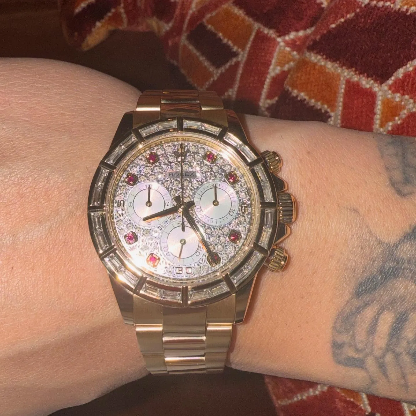 Drake wearing a diamond-encrusted Rolex with a gold band and red gems.