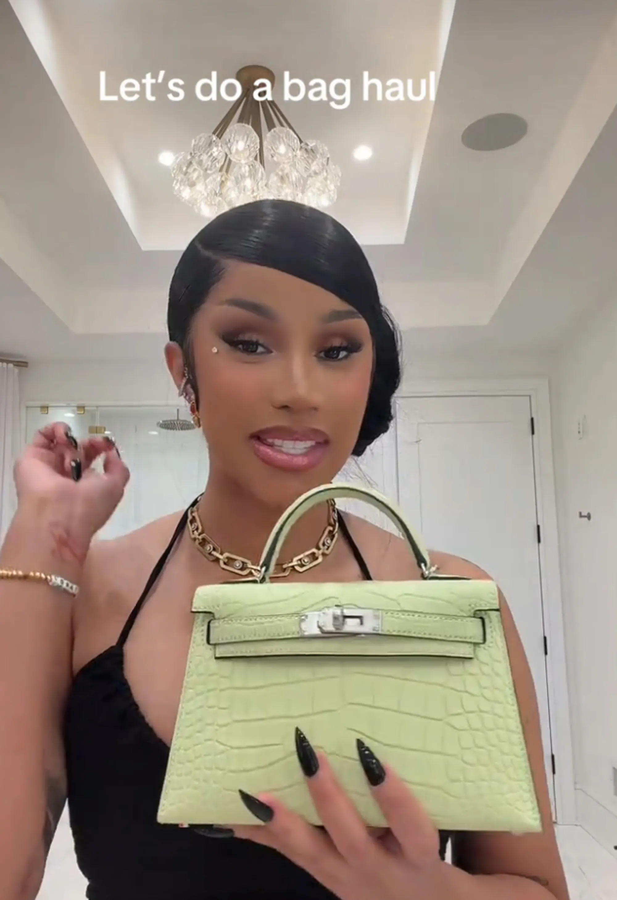 Cardi B holds up a light green Hermès Mini Kelly bag.