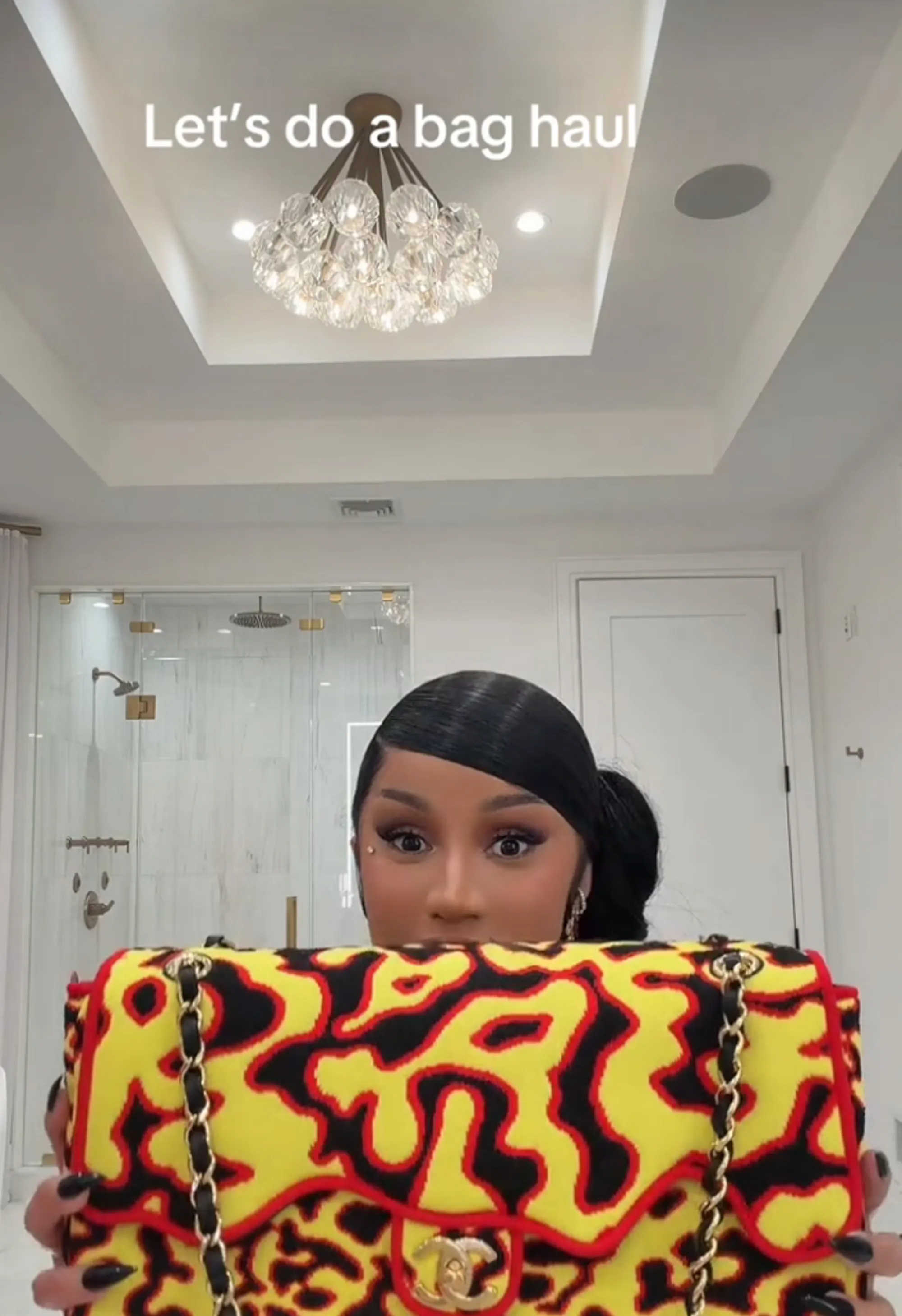 Cardi B peeks over a yellow, black, and red Chanel bag with a gold chain strap.