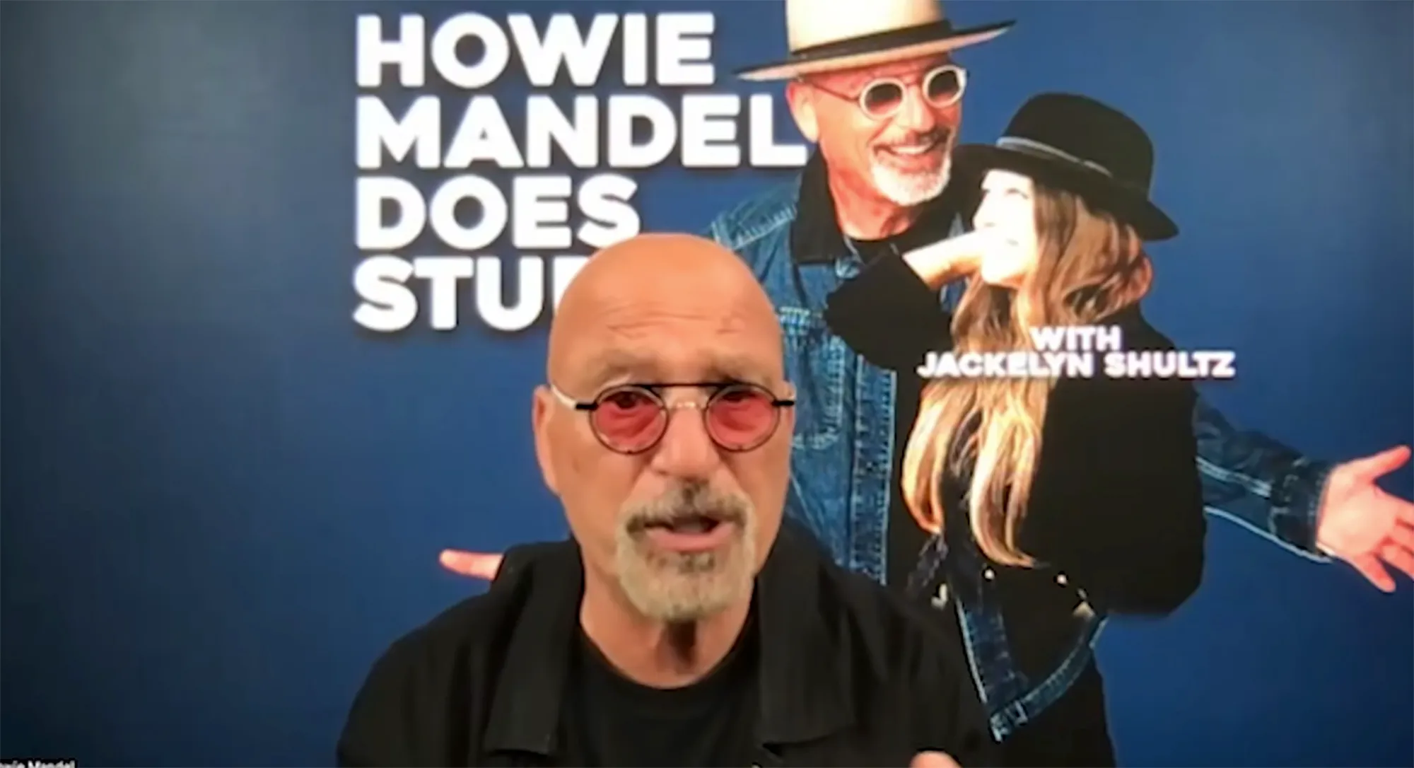Howie Mandel speaking in front of a poster for "Howie Mandel Does Stuff" with Jackelyn Shultz.