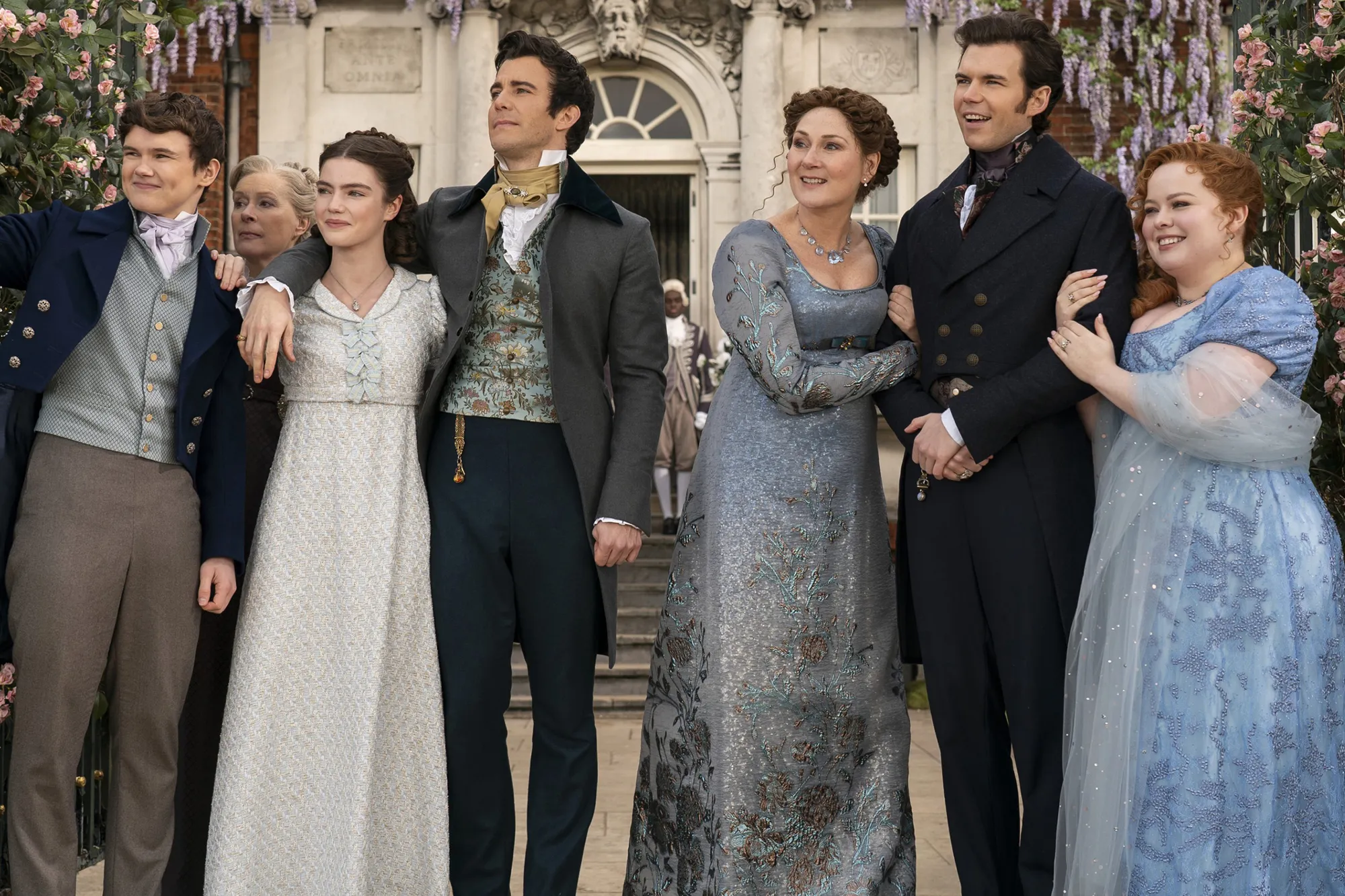Six actors in period clothing, standing outside a large house.