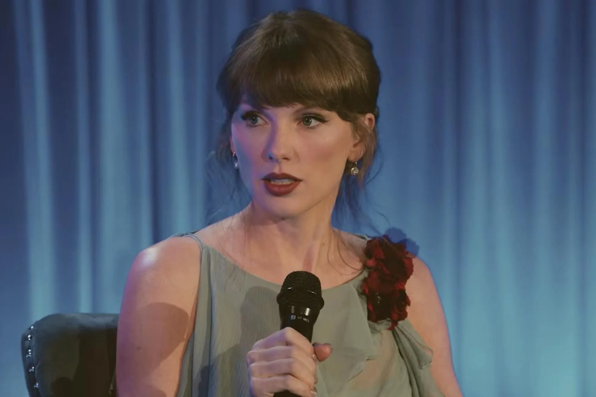 Taylor Swift holding a microphone, speaking at an event.