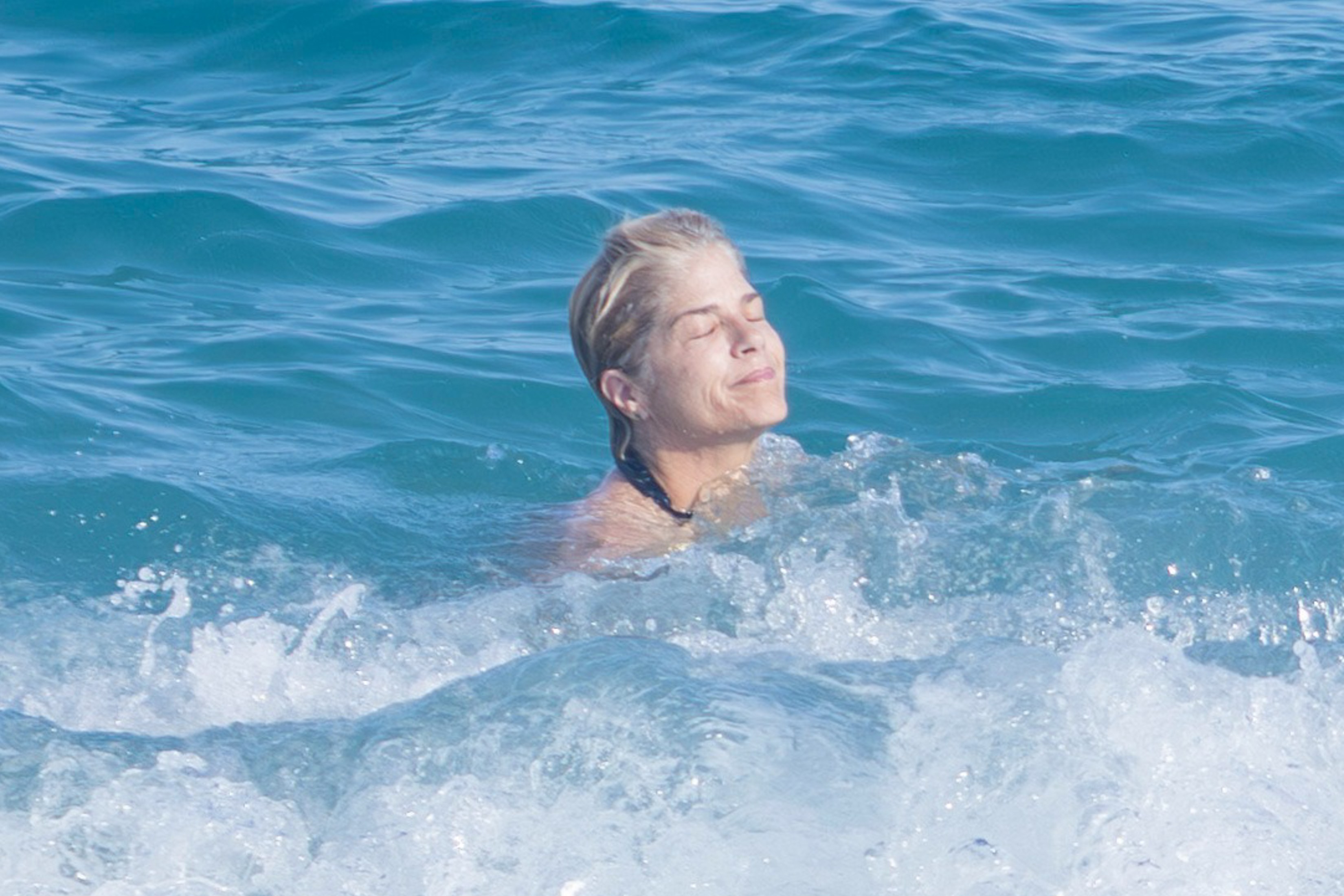 Selma Blair with her eyes closed, partially submerged in the ocean with waves crashing around her.