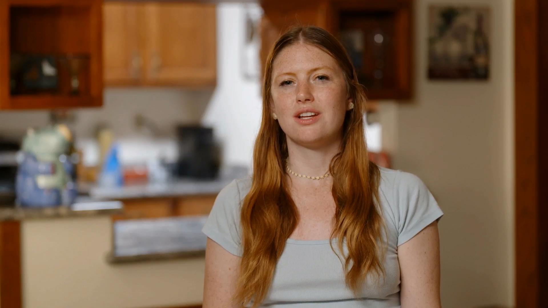 Catie, from 90 Day Fiance, with long red hair and a light blue shirt, looks to the right.
