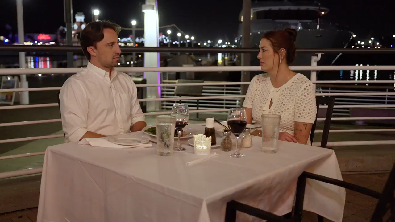 Paula and Thomas from 90 Day Fiance sitting at an outdoor restaurant table at night.