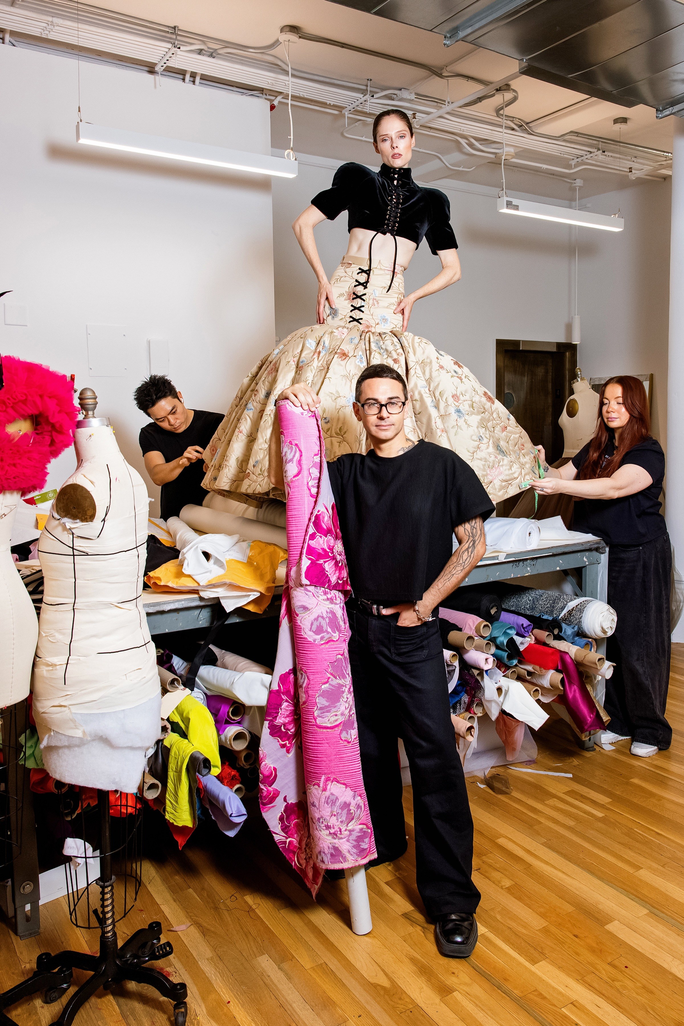 Christian Siriano in his fashion design studio with a model, another designer, and a seamstress.