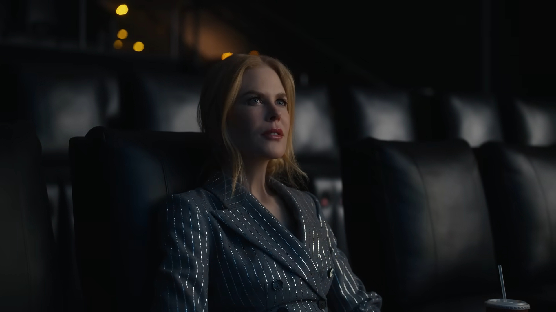 Nicole Kidman in a striped suit watches a movie in a dark theater.