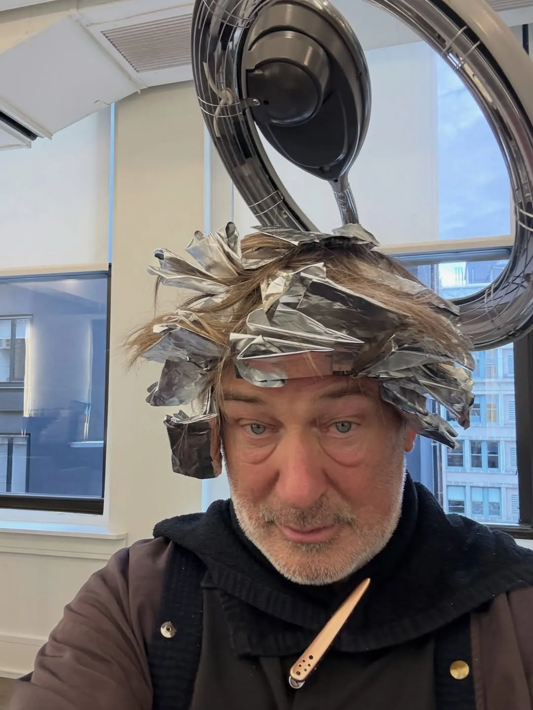 Alec Baldwin with hair foils under a hair dryer.