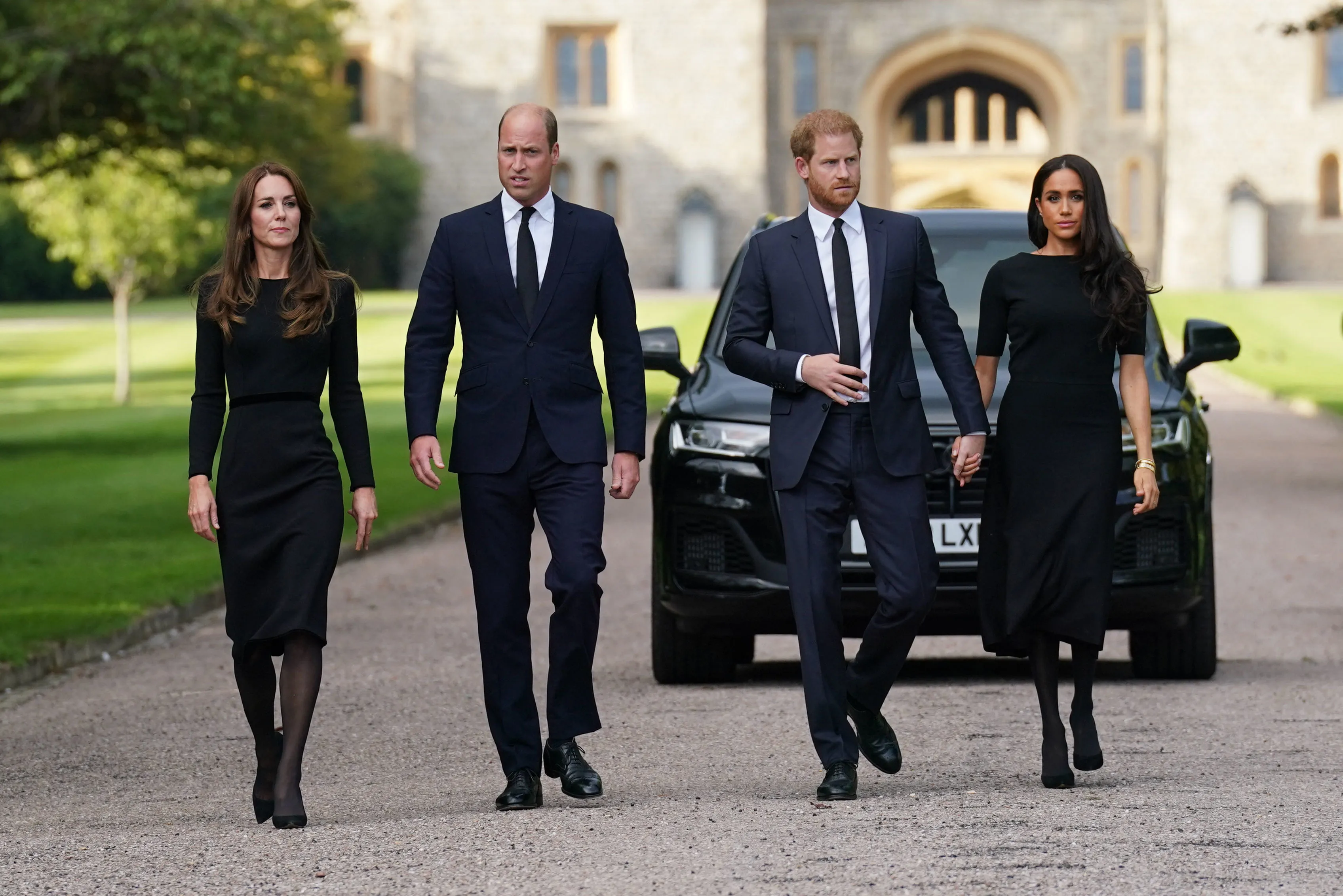 Catherine, Princess of Wales, Prince William, Prince of Wales, Prince Harry, Duke of Sussex, and Meghan, Duchess of Sussex, walk together in black funeral attire.