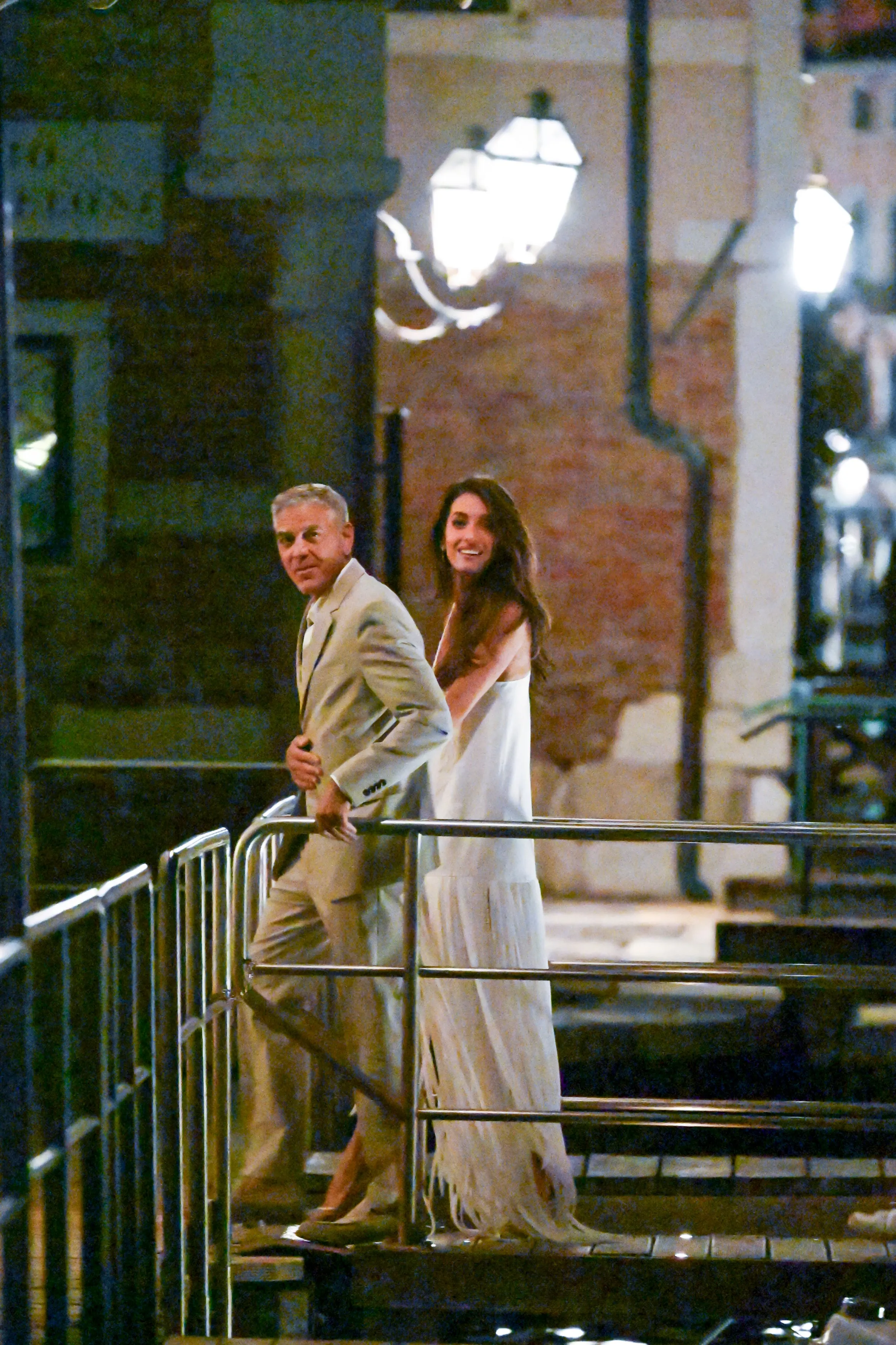 George and Amal Clooney, dressed in formal wear, on a Venice bridge at night.