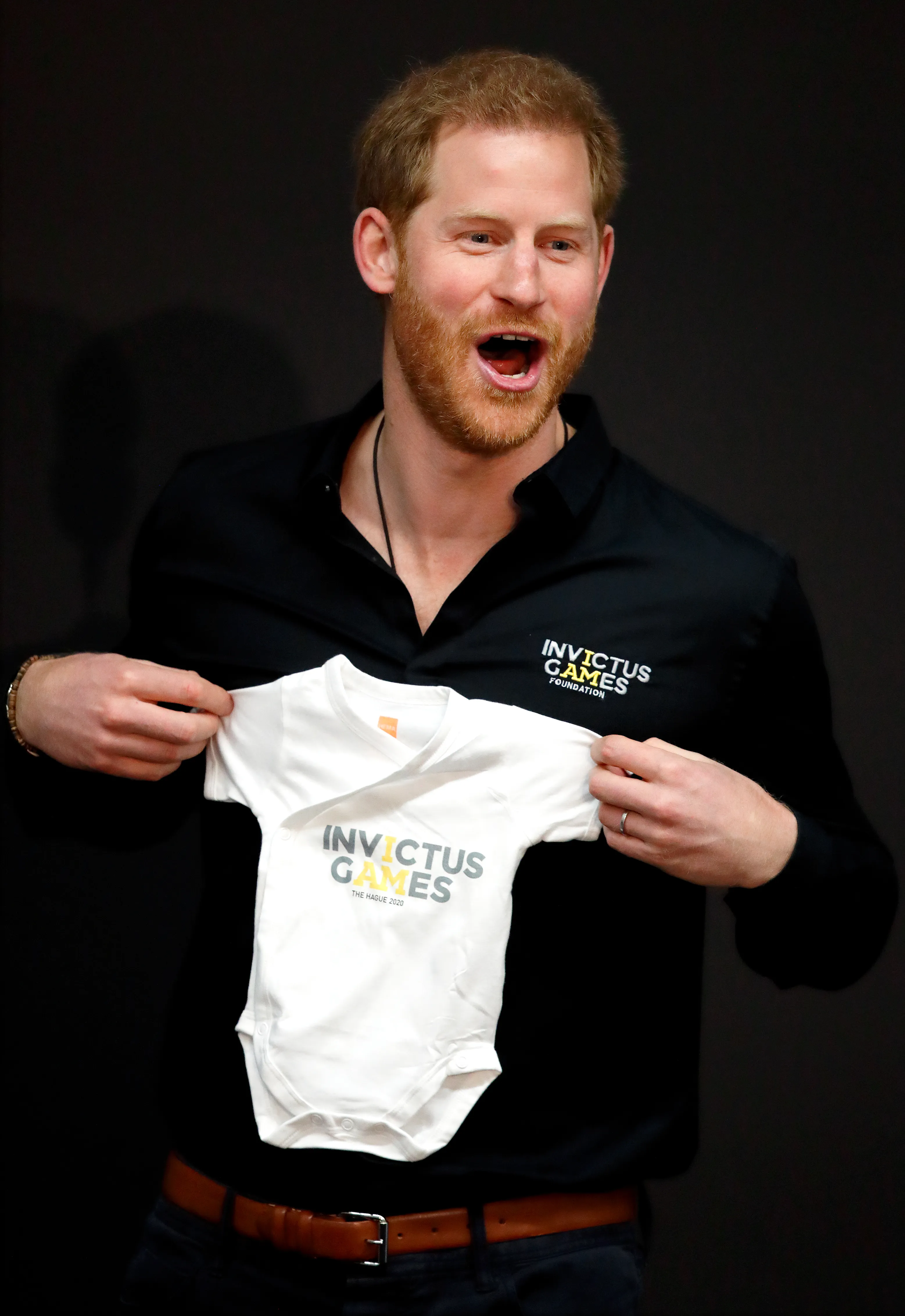 Prince Harry holding up a white babygrow that says "Invictus Games, The Hague 2020."