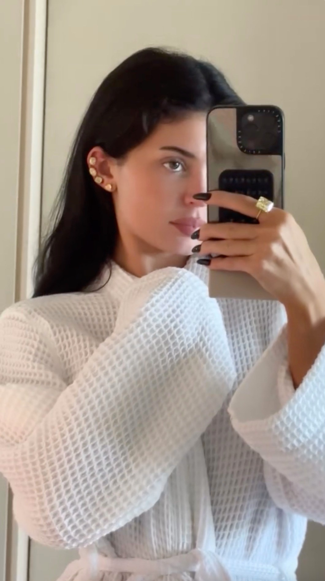 Kylie Jenner taking a mirror selfie, wearing diamond earrings and a large diamond ring.