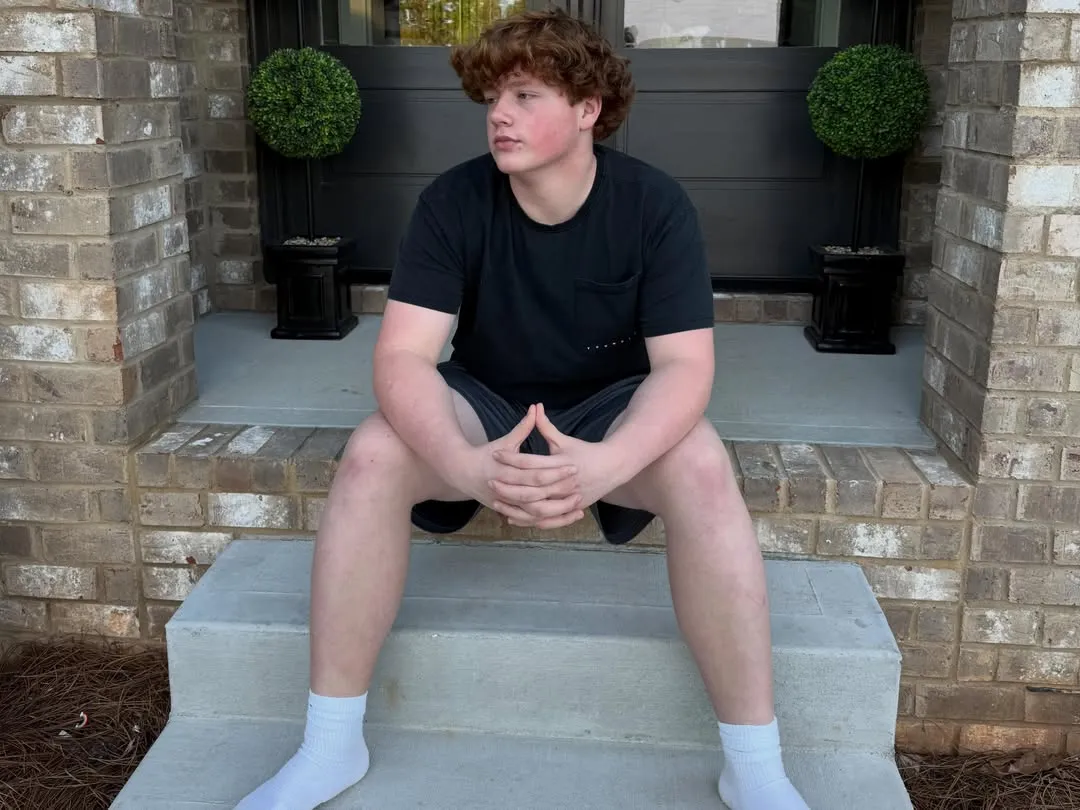 KJ Biermann, son of Kim Zolciak, sitting on outdoor steps.