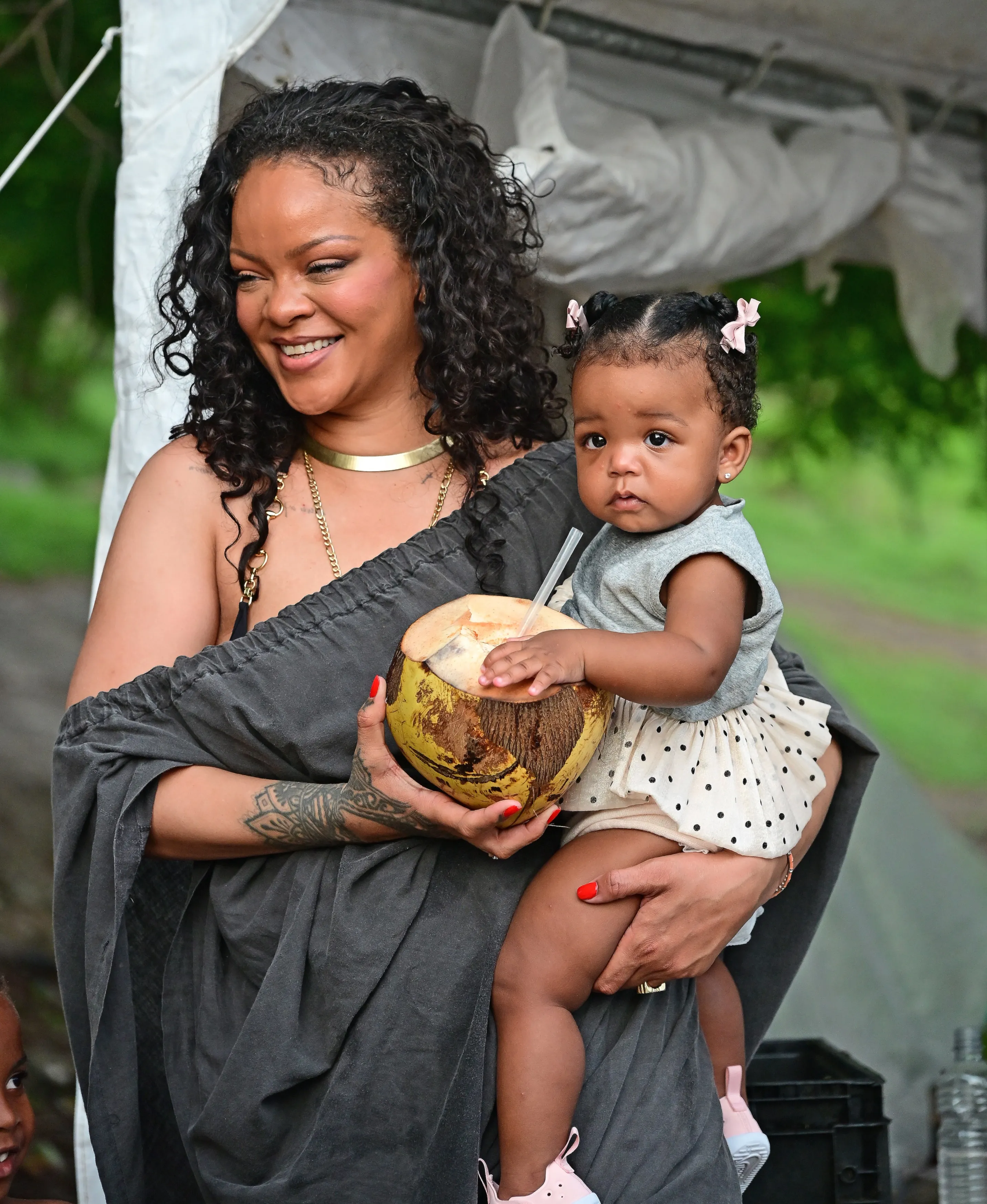 Rihanna holds Rocki, who sips from a coconut with a straw.