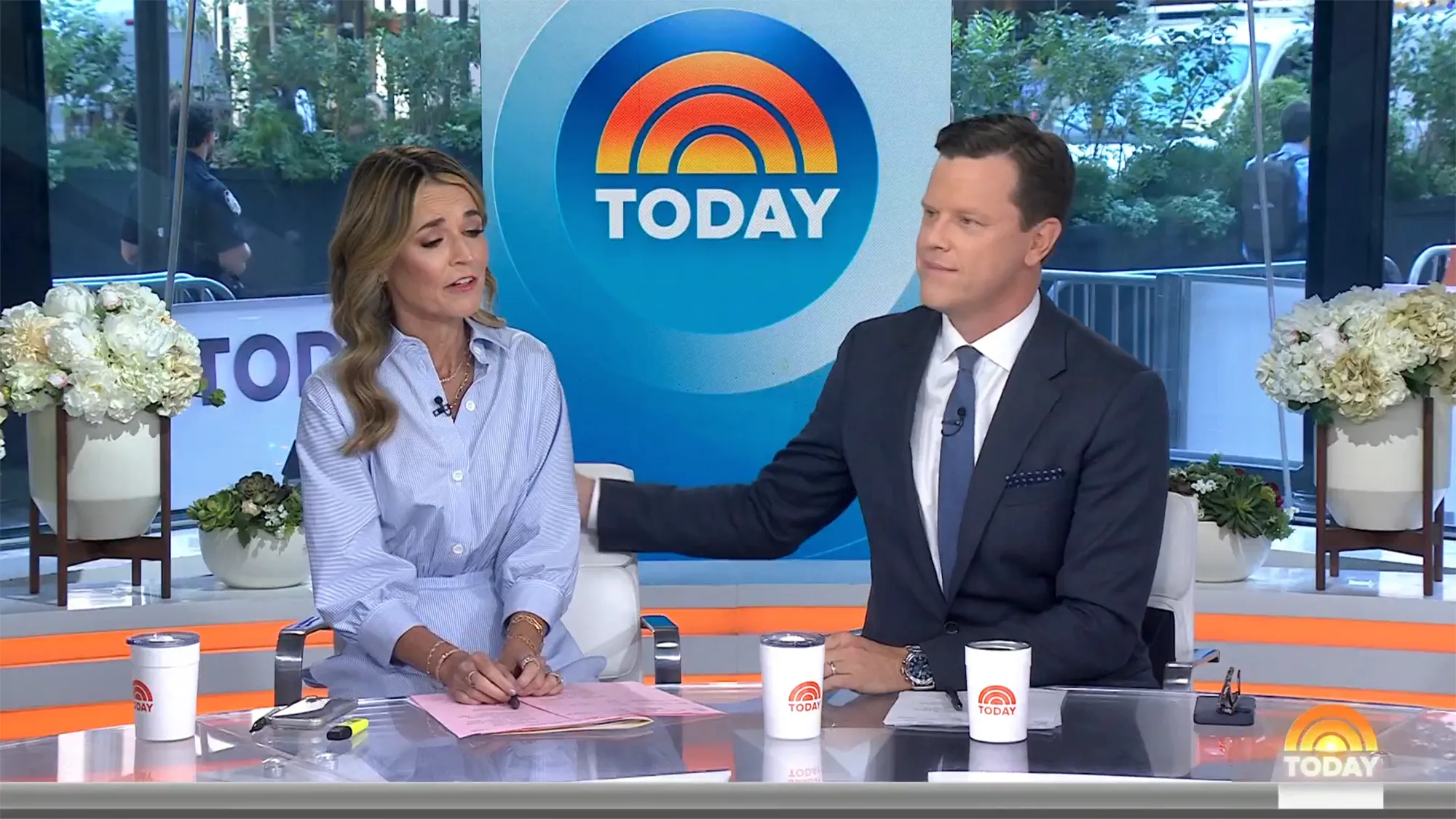 Savannah Guthrie sitting at a desk with a man in a suit, both looking toward the left.