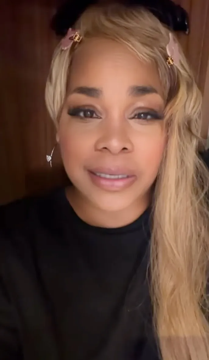 T-Boz Watkins, with long blonde hair and two pink butterfly clips, looks directly into the camera.