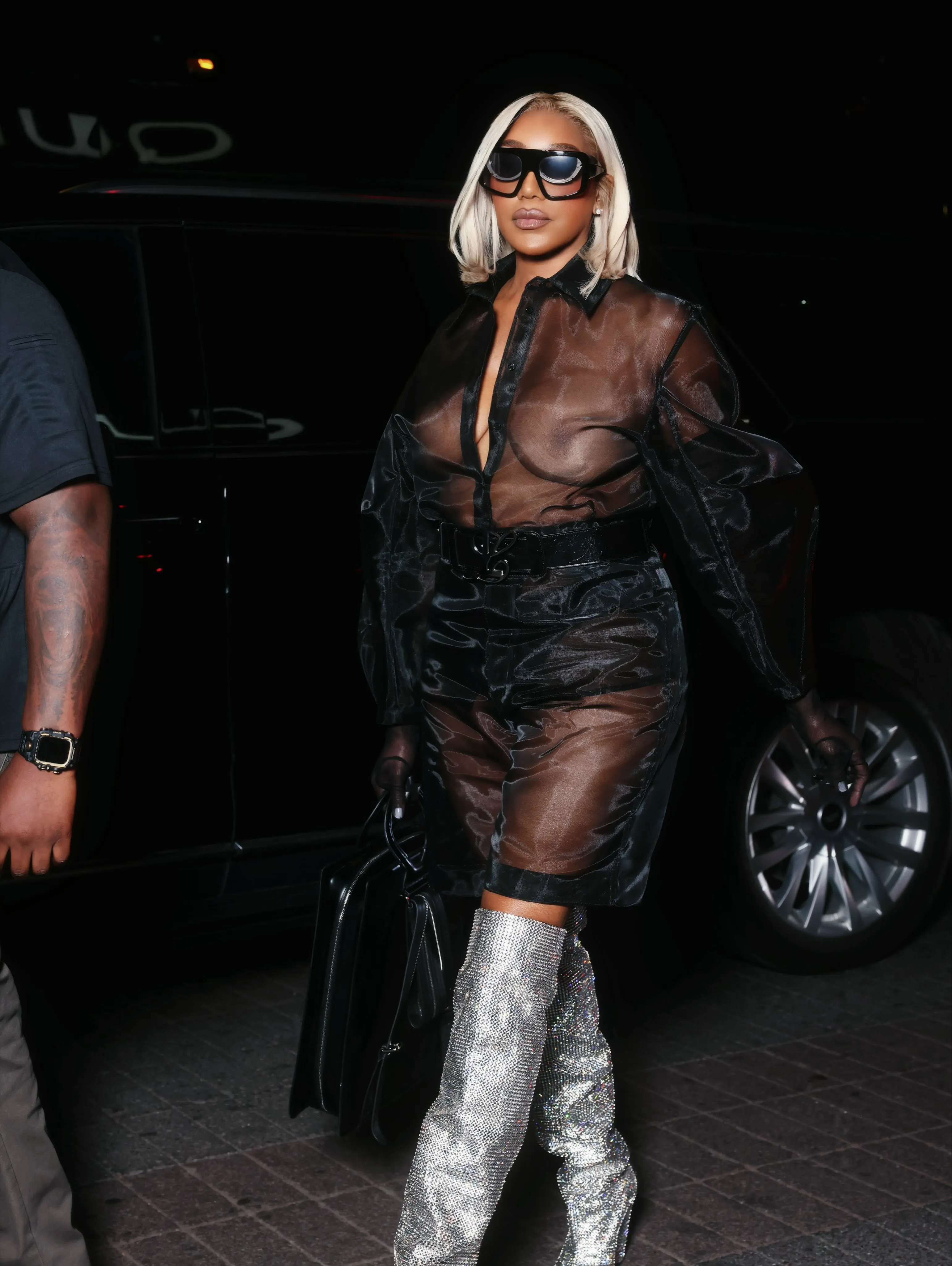 NeNe Leakes in a sheer black shirt, black shorts, and glittery thigh-high boots, arriving at the Luar show during NYFW.