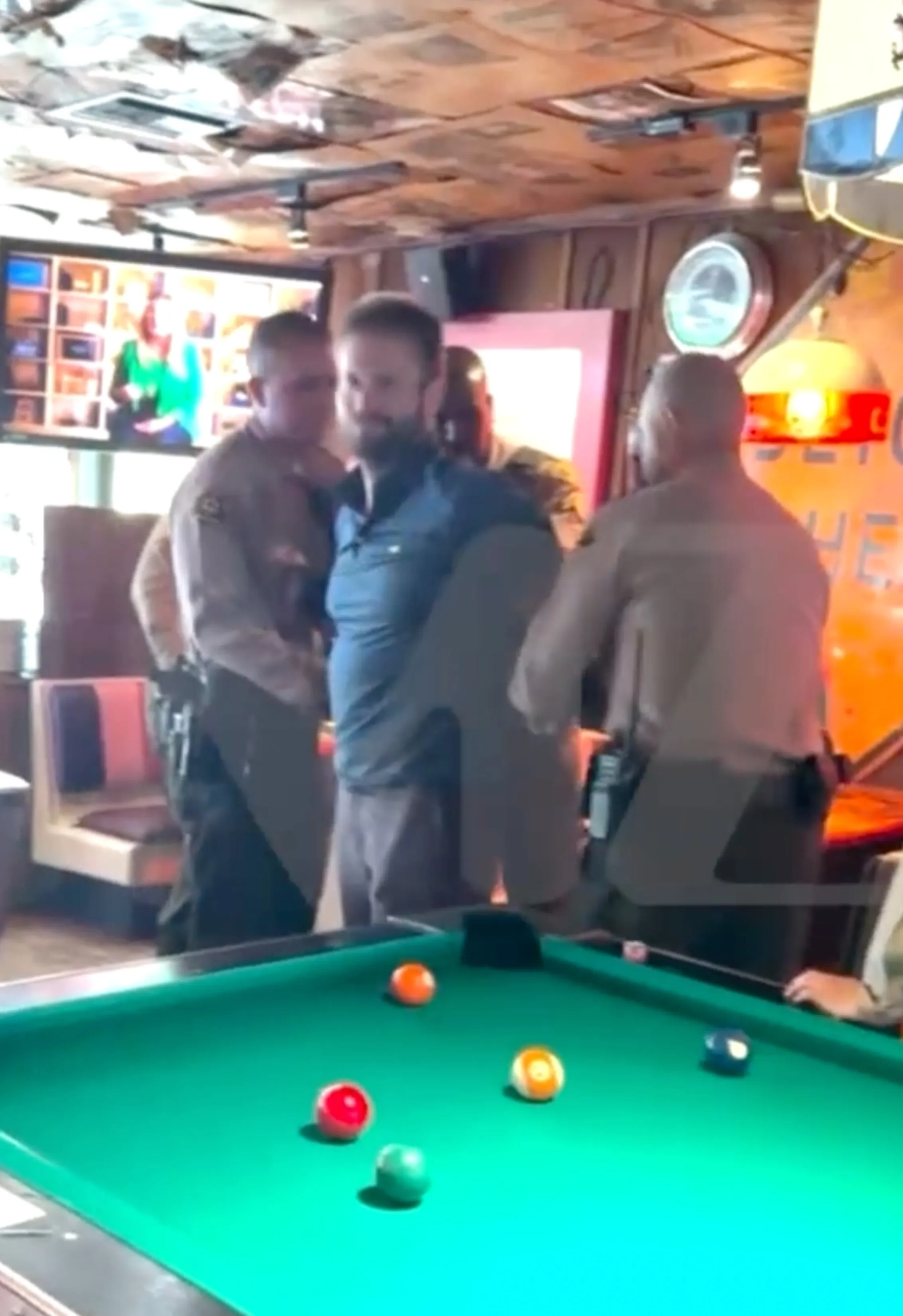 Police arresting Brian Hickerson in a bar with a pool table in the foreground.