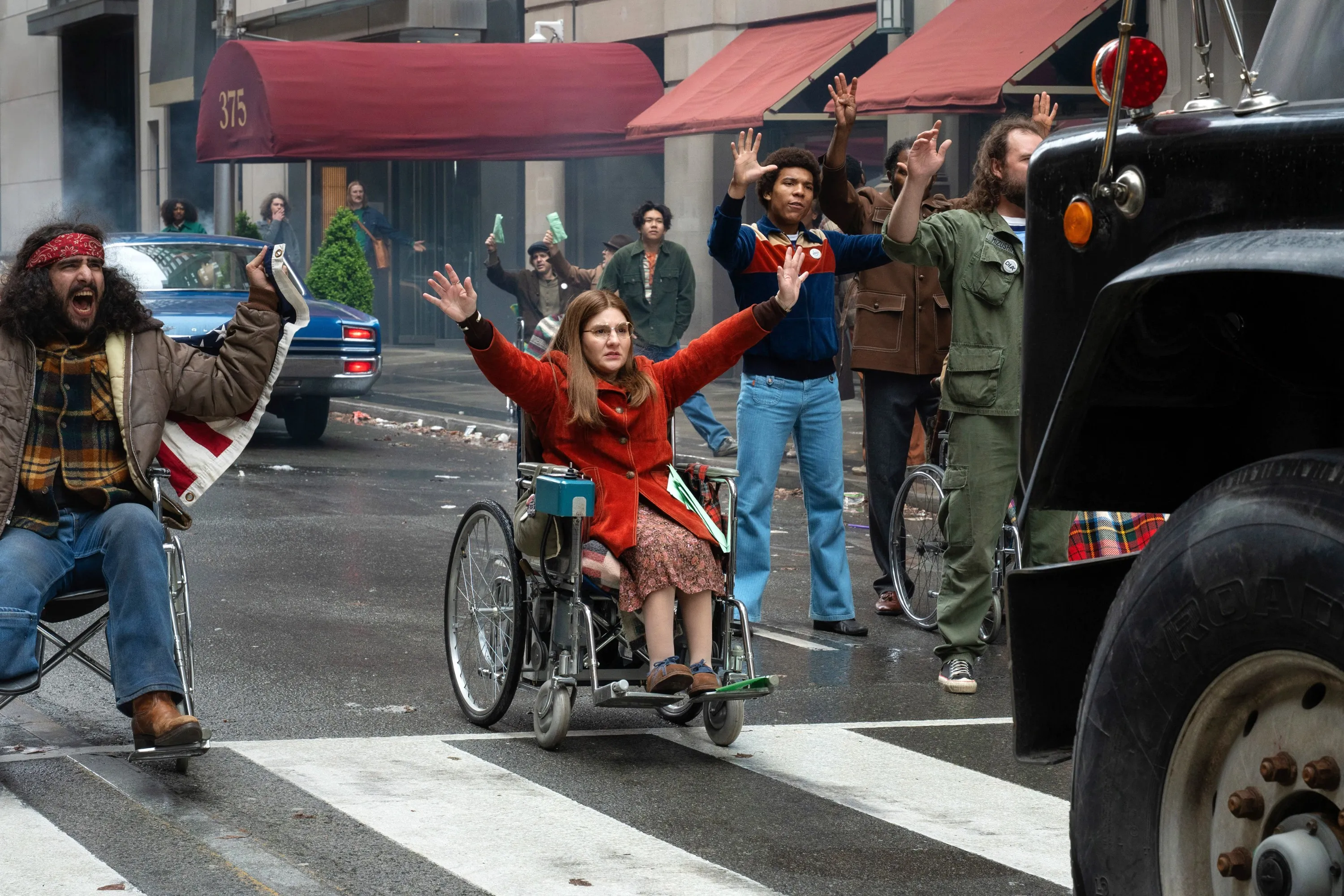 Ruth Madeley as Judy Heumann in a wheelchair protesting with a group of people in the street.